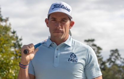 Scott Stallings holding a golf club on his shoulder, wearing a white Titleist hat and a tasc collared shirt.