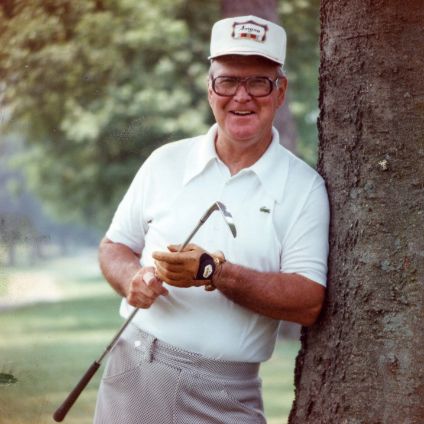 Waxo Green holding a golf club while leaning against a tree